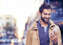 homme au milieu de la rue regardant son téléphone portable en souriant