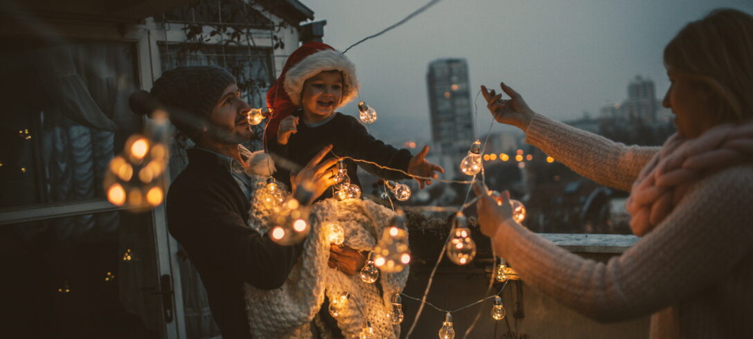 Jeune famille s'amusant ensemble sur la terrasse de leur appartement, décorant pour les vacances de Noël