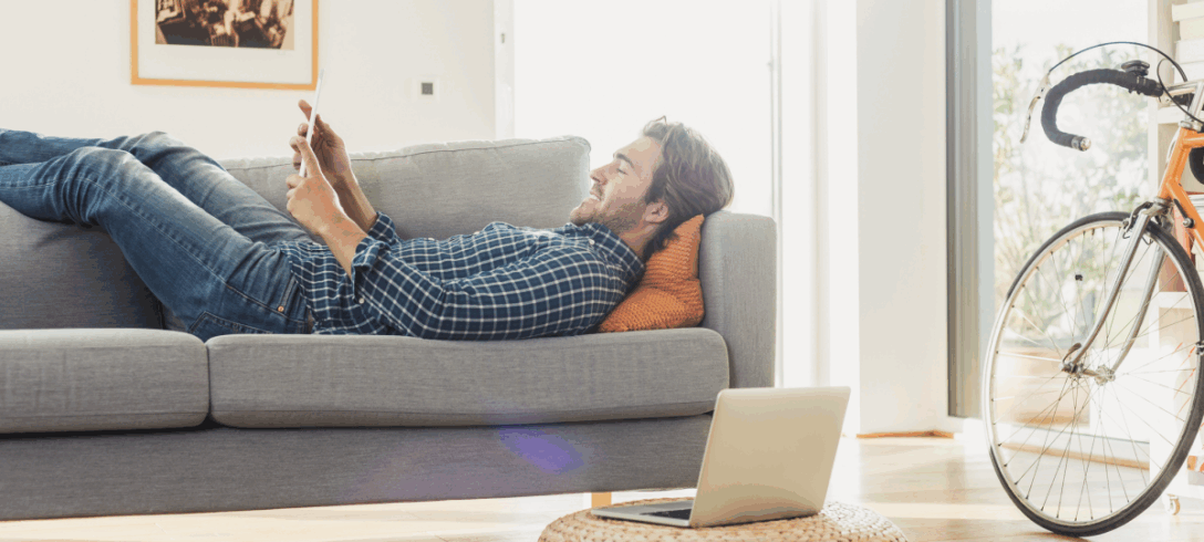 homme allongé sur un canapé dans le salon avec tablette à la main