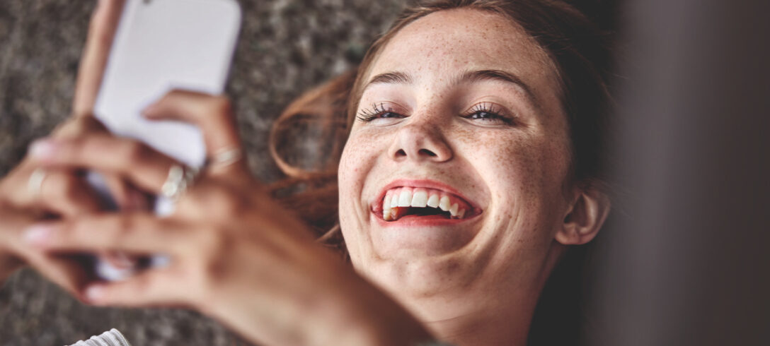 jeune femme allongée sur le sol, heureuse tout en envoyant une conversation sur un téléphone portable