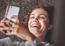 jeune femme allongée sur le sol, heureuse tout en envoyant une conversation sur un téléphone portable