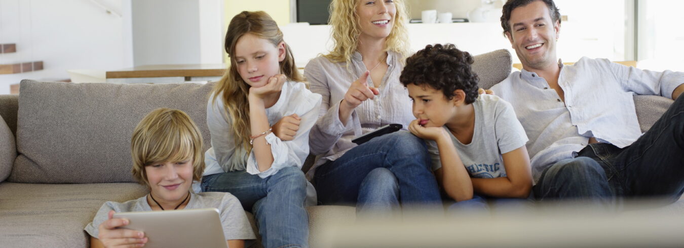 Famille ensemble sur le canapé du salon. Les parents regardent la télévision et les enfants jouent sur la tablette