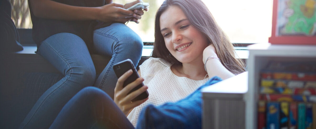 Adolescent textos sur téléphone portable dans la bibliothèque de l'école