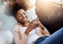 jeune femme envoyant des SMS sur un téléphone portable allongé sur un canapé