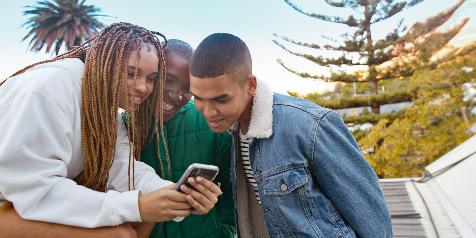 Femme souriante montrant un téléphone portable à des amis masculins sur la terrasse