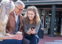 fille montrant une photo sur son téléphone portable à ses parents assis sur un banc de rue