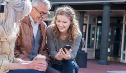 fille montrant une photo sur son téléphone portable à ses parents assis sur un banc de rue