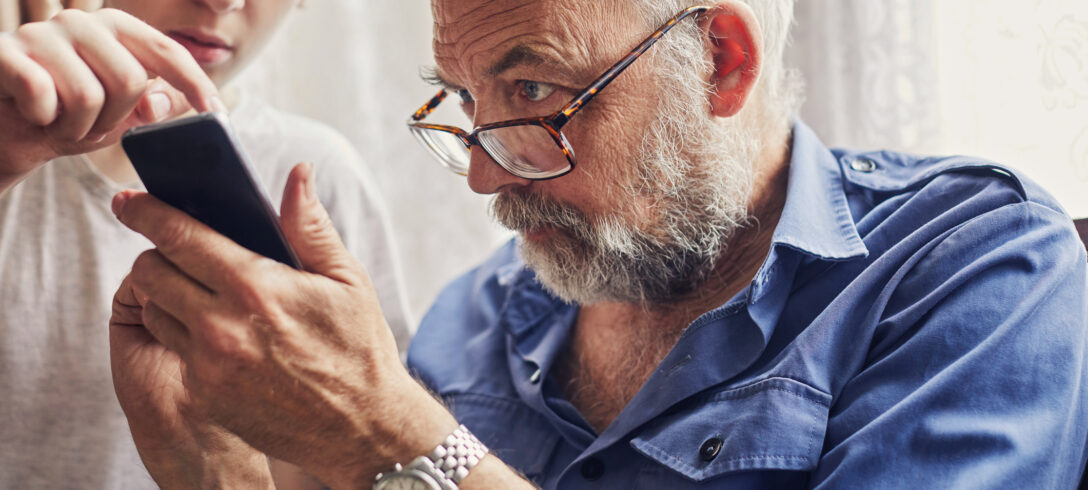 petit-fils apprenant à son grand-père à utiliser le téléphone portable