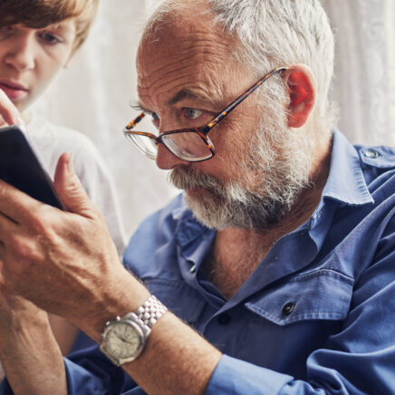 petit-fils apprenant à son grand-père à utiliser le téléphone portable