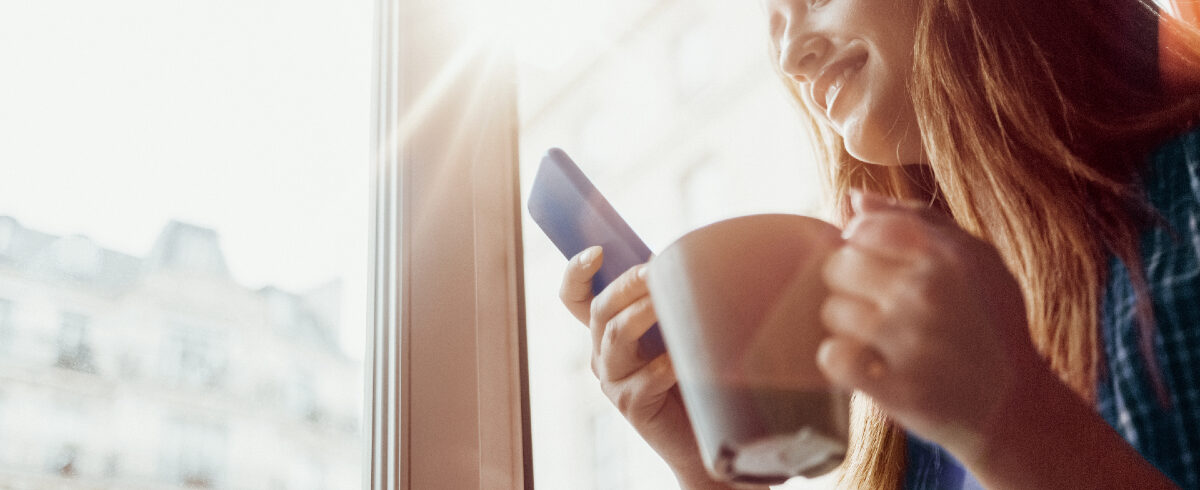 femme à la fenêtre de la maison buvant du café tout en envoyant des SMS