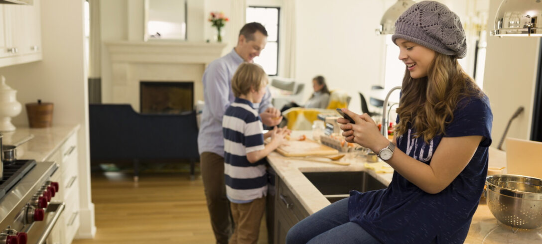 le père et les petits enfants préparent le déjeuner pendant que la fille est assise sur l'île en envoyant des messages sur le téléphone portable