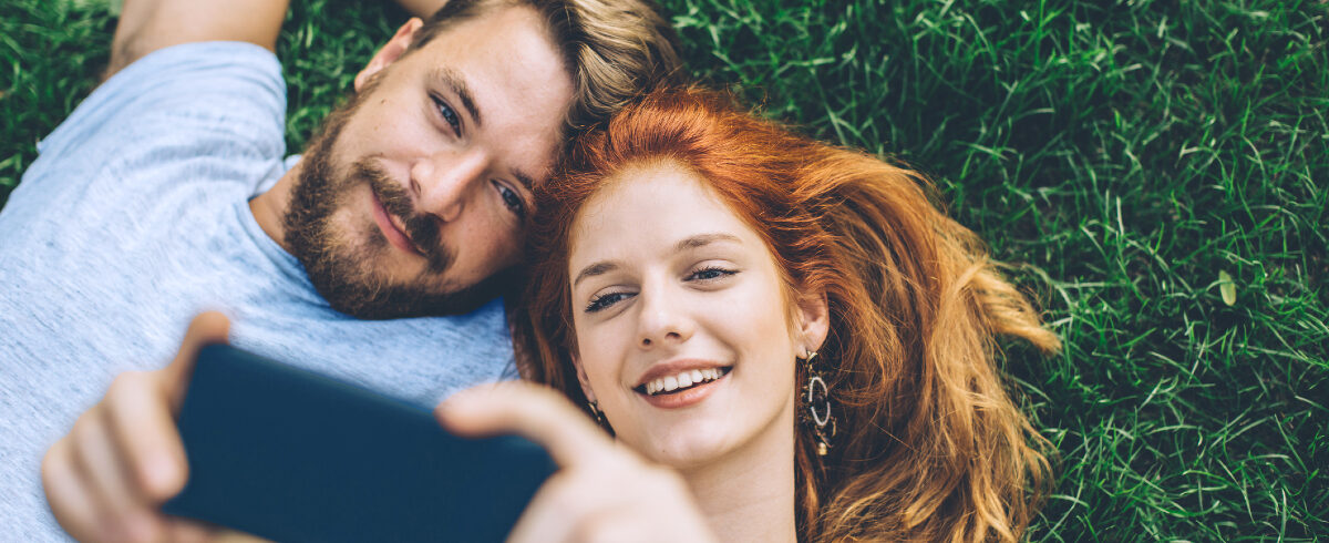 couple allongé sur l'herbe prenant un selfie