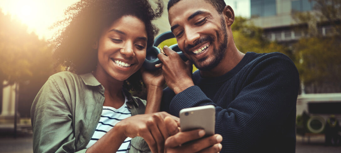 couple souriant regardant le téléphone portable tout en écoutant de la musique avec les mêmes écouteurs