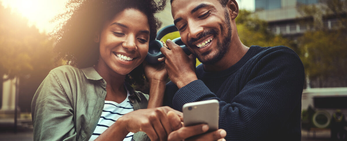 couple souriant regardant le téléphone portable tout en écoutant de la musique avec les mêmes écouteurs