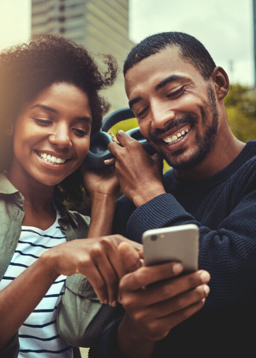 couple souriant regardant le téléphone portable tout en écoutant de la musique avec les mêmes écouteurs