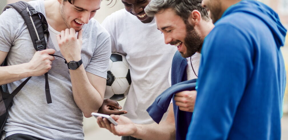 Groupe de jeunes hommes sportifs urbains s'amusant avec un téléphone intelligent au parc de la ville