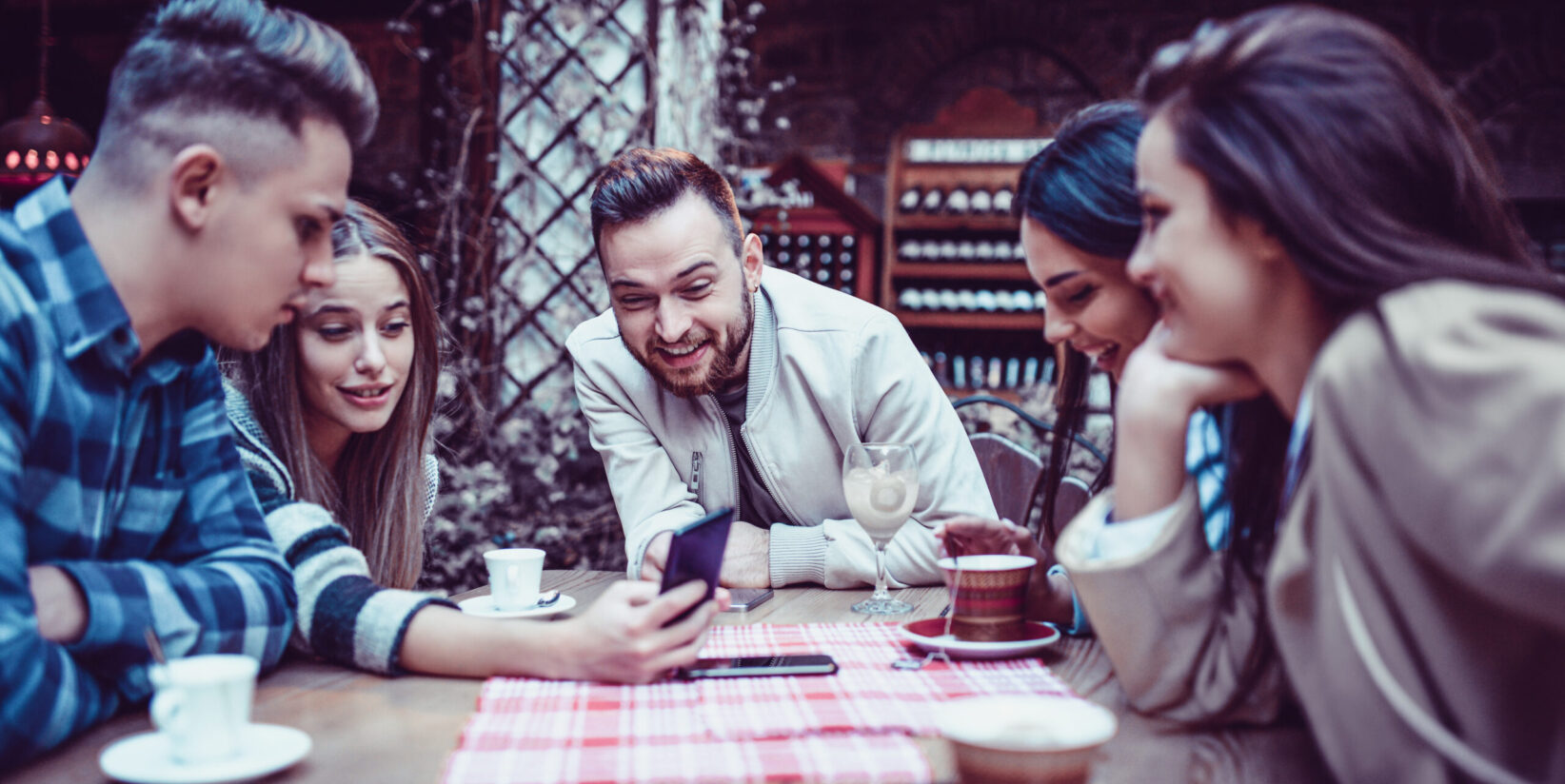 Groupe d'amis souriants regardant un smartphone dans un restaurant de café traditionnel