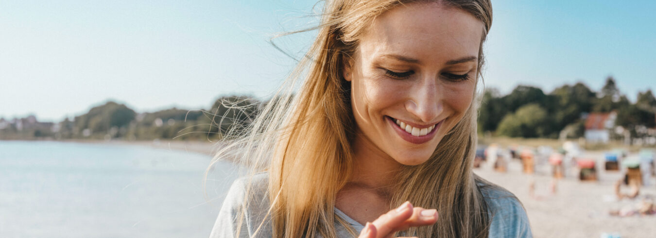 gros plan d'une jeune femme souriante utilisant son téléphone portable avec la plage en arrière-plan