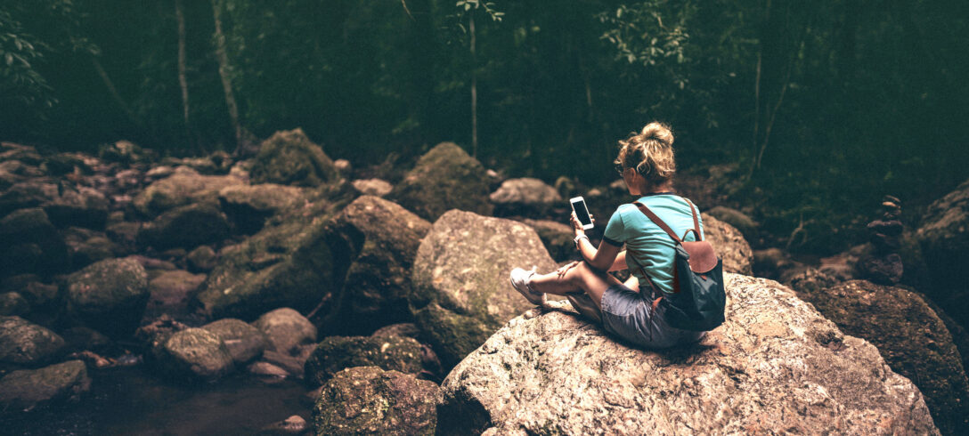 jeune femme au milieu de la forêt seule assise sur un rocher consultant son téléphone portable