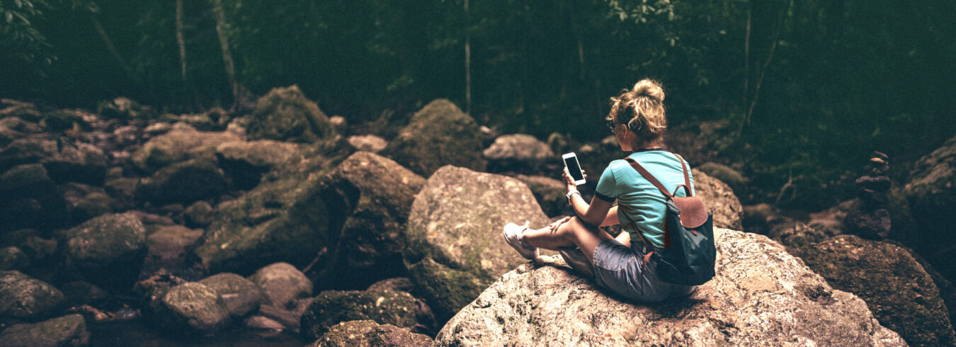 jeune femme au milieu de la forêt seule assise sur un rocher consultant son téléphone portable