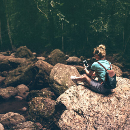 jeune femme au milieu de la forêt seule assise sur un rocher consultant son téléphone portable