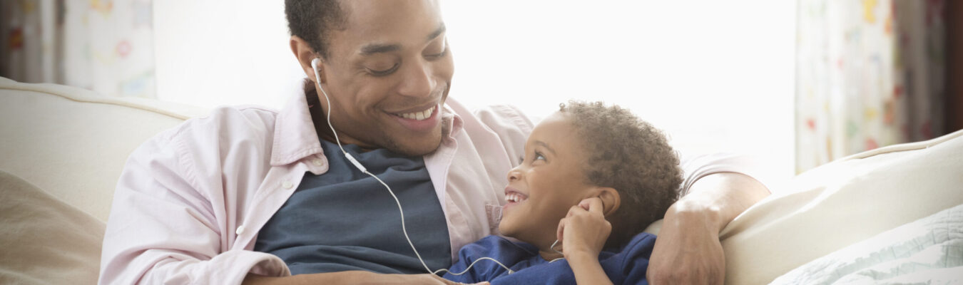 Père et fils de race mixte écoutant des écouteurs sur un canapé