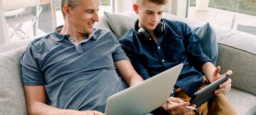 père et fils assis sur le canapé en regardant une vidéo sur leurs appareils portables