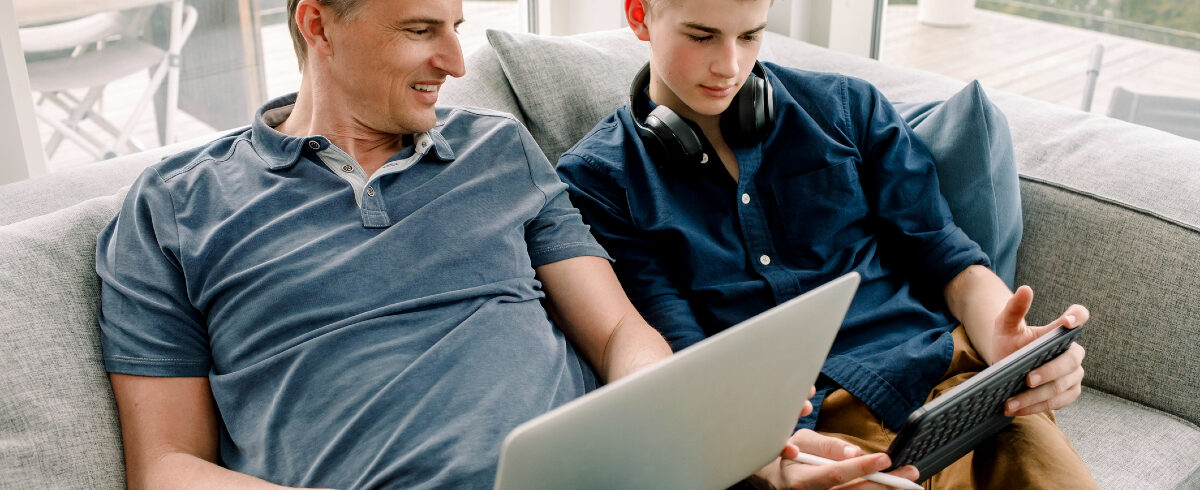 père et fils assis sur le canapé en regardant une vidéo sur leurs appareils portables