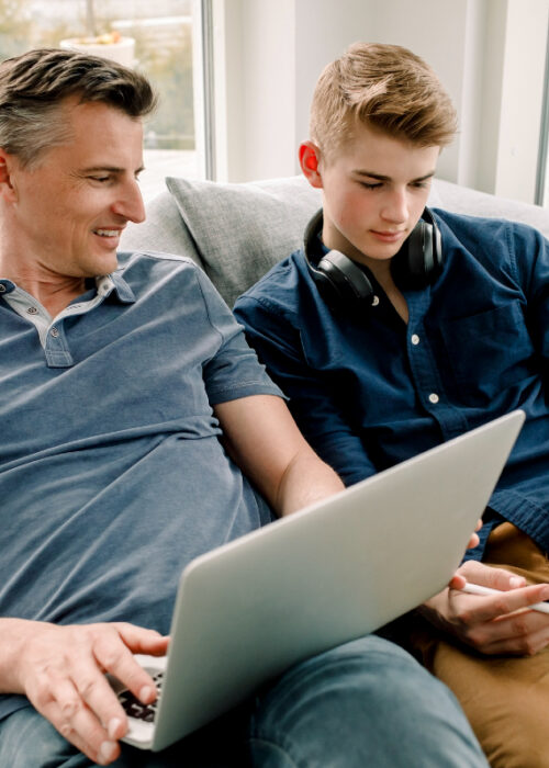 père et fils assis sur le canapé en regardant une vidéo sur leurs appareils portables