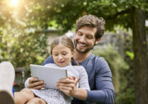 Happy father and daughter using tablet together in garden