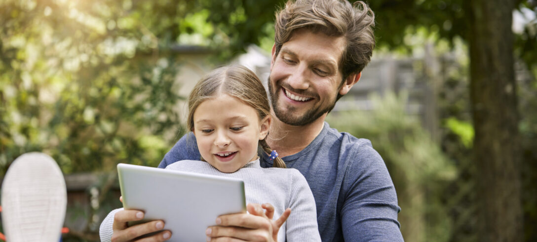Happy father and daughter using tablet together in garden