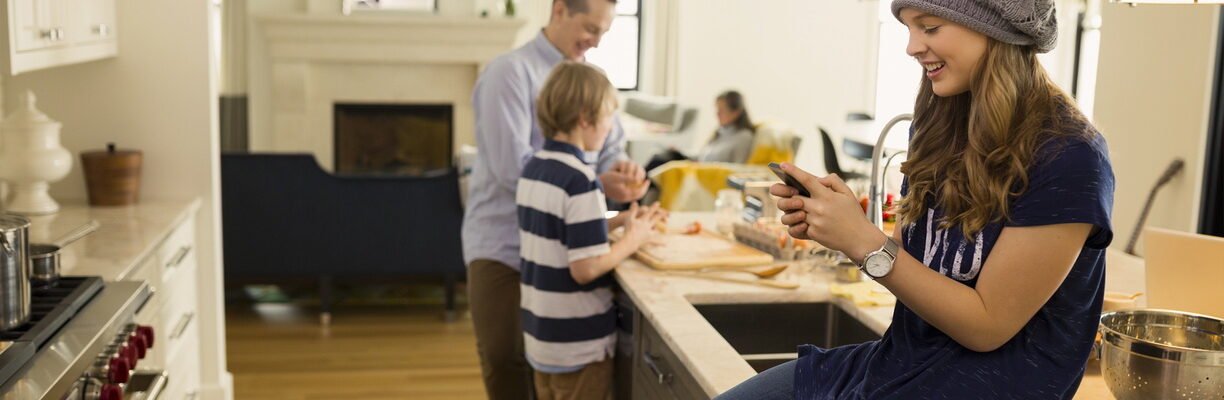 père et fils préparant le déjeuner, la mère assise sur le canapé et la fille assise sur le comptoir de la cuisine sur le téléphone portable