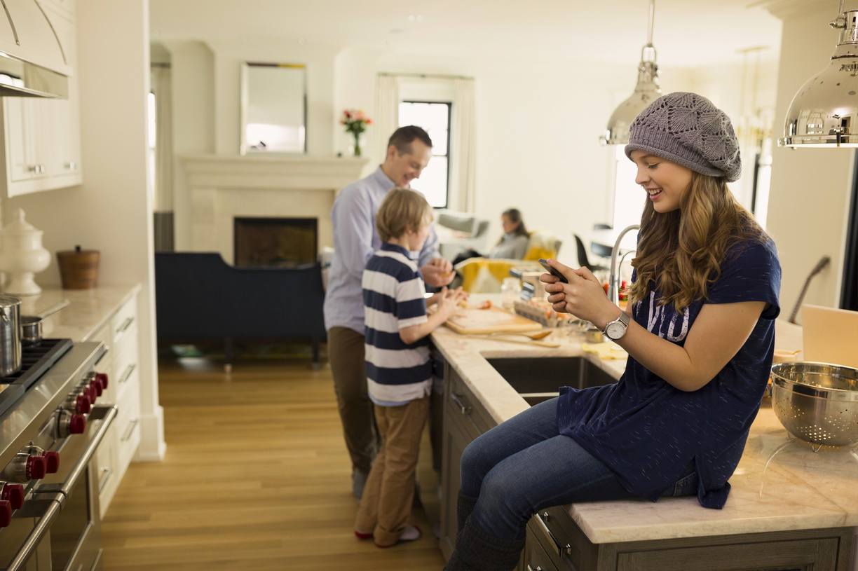 père et fils préparant le déjeuner, la mère assise sur le canapé et la fille assise sur le comptoir de la cuisine sur le téléphone portable