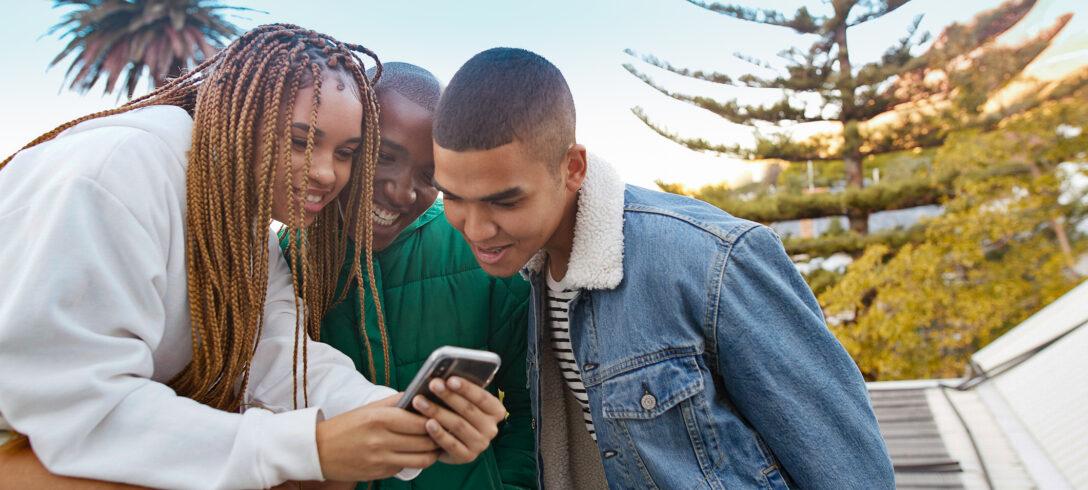 Femme souriante montrant un téléphone portable à des amis masculins sur la terrasse