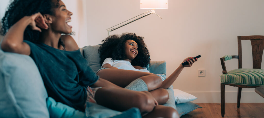 deux femmes riant en regardant la télévision allongées sur le canapén