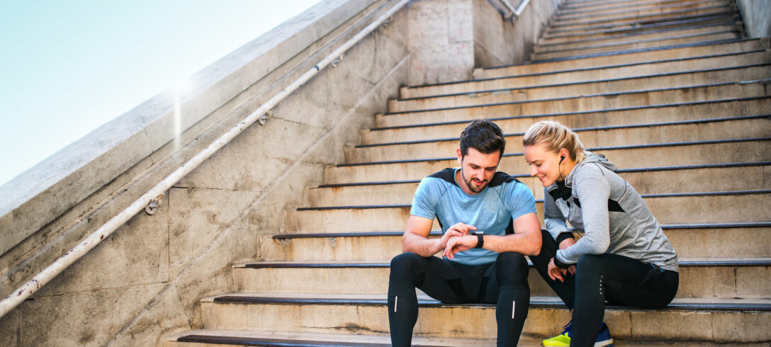 Un homme et une femme sportifs assis sur les marches regardent une montre intelligente