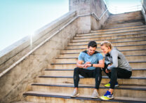 Un homme et une femme sportifs assis sur les marches regardent une montre intelligente