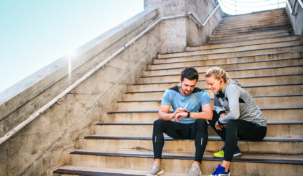 Un homme et une femme sportifs assis sur les marches regardent une montre intelligente