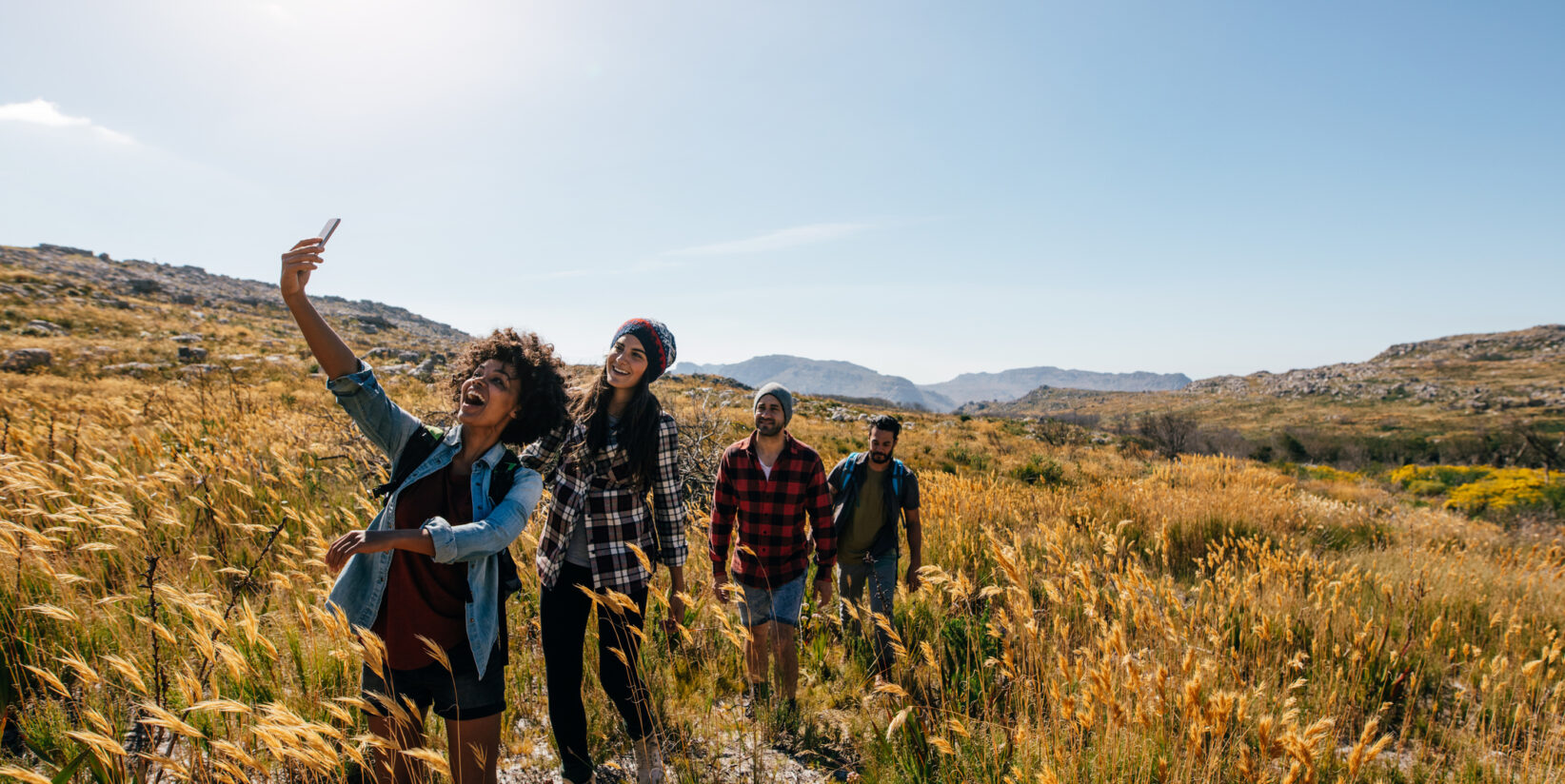 Jeunes hommes et femmes faisant de la randonnée dans la campagne et prenant un selfie avec un smartphone.