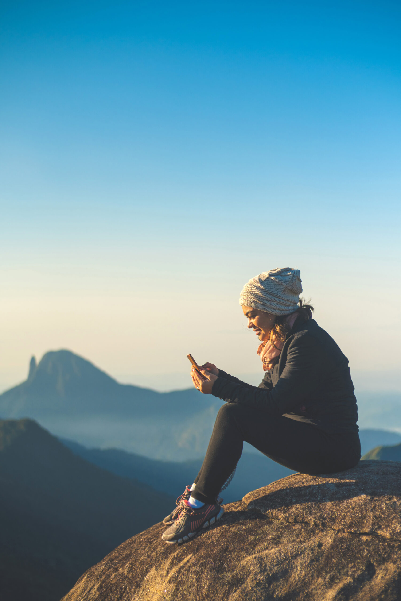 une femme assise au sommet d'une montagne regardant son téléphone portable