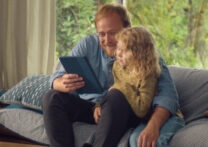 père et fille assis sur un canapé en regardant une tablette