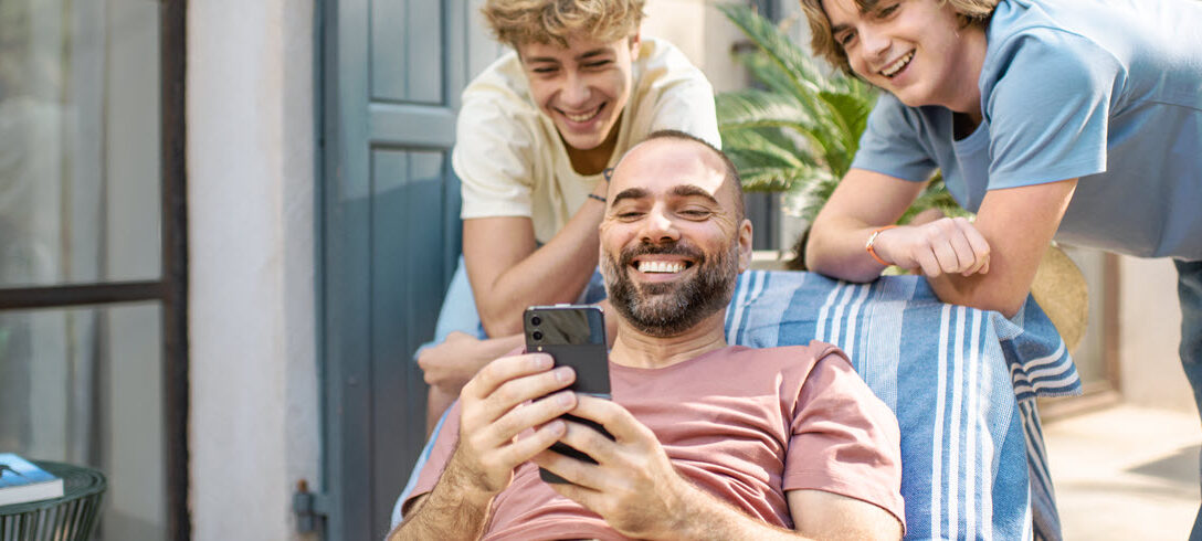 1 homme et 2 jeunes rient en regardant quelque chose sur leur téléphone portable