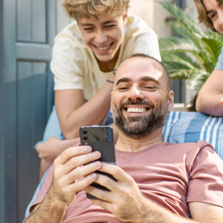 1 homme et 2 jeunes rient en regardant quelque chose sur leur téléphone portable