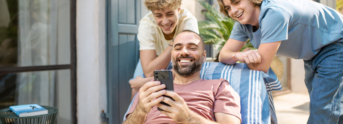 1 homme et 2 jeunes rient en regardant quelque chose sur leur téléphone portable