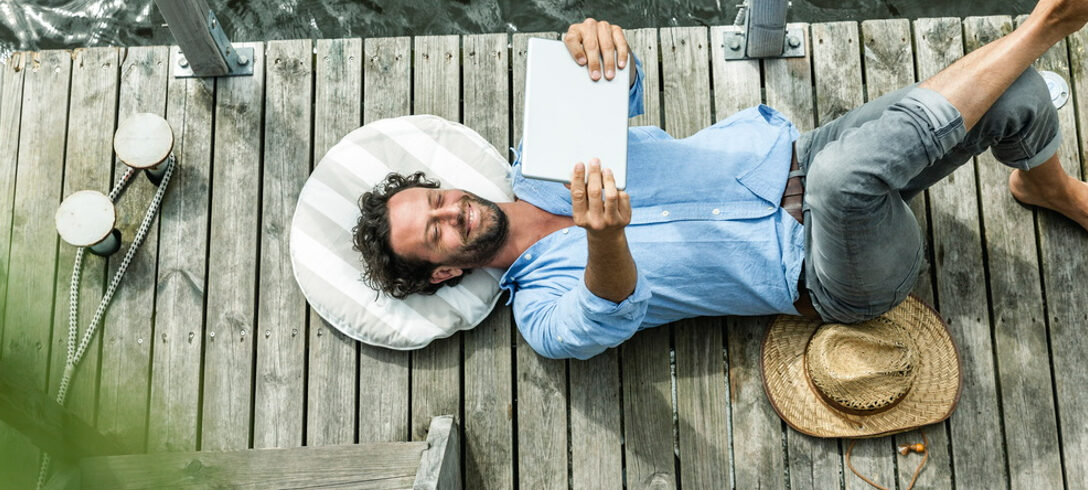 homme allongé à l'aide d'une tablette sur le ventre au bord d'un lac
