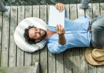 homme allongé à l'aide d'une tablette sur le ventre au bord d'un lac