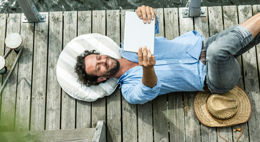 homme allongé à l'aide d'une tablette sur le ventre au bord d'un lac