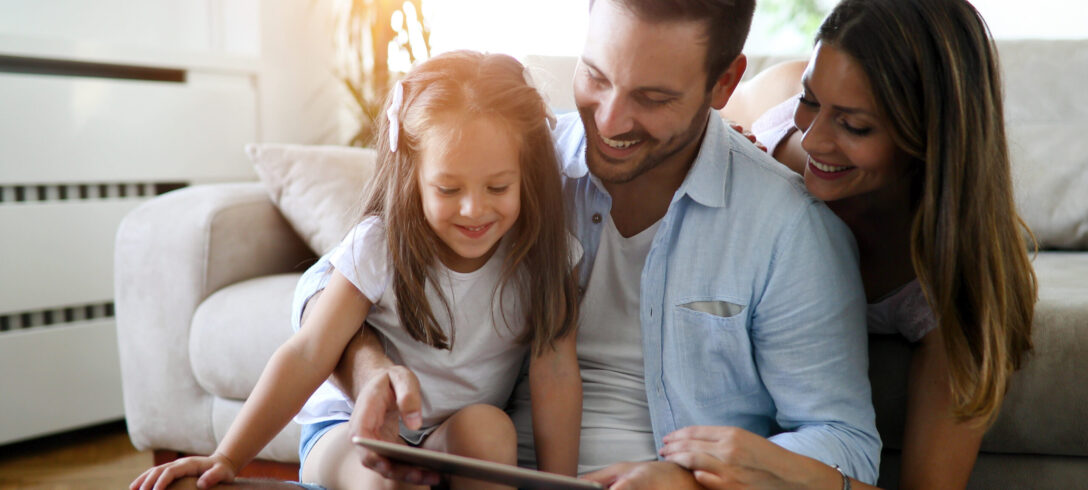 père et mère assis par terre avec leur jeune fille dans les bras tout en utilisant la tablette