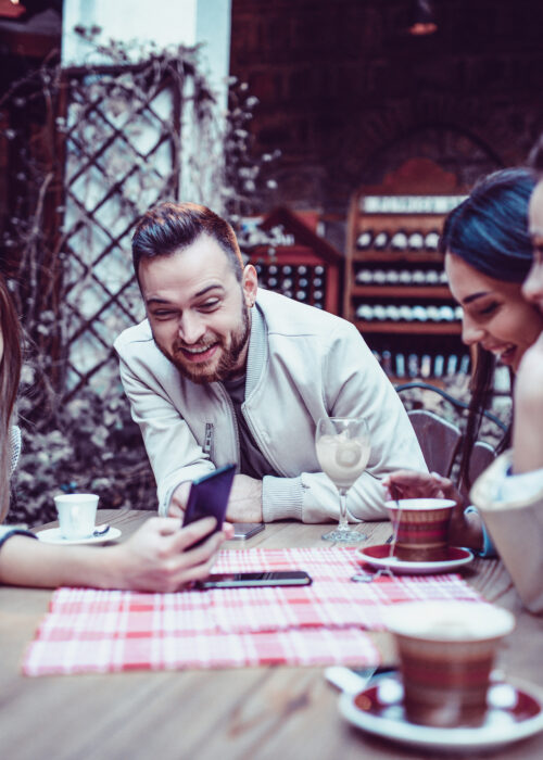Groupe d'amis souriants regardant un smartphone dans un restaurant de café traditionnel