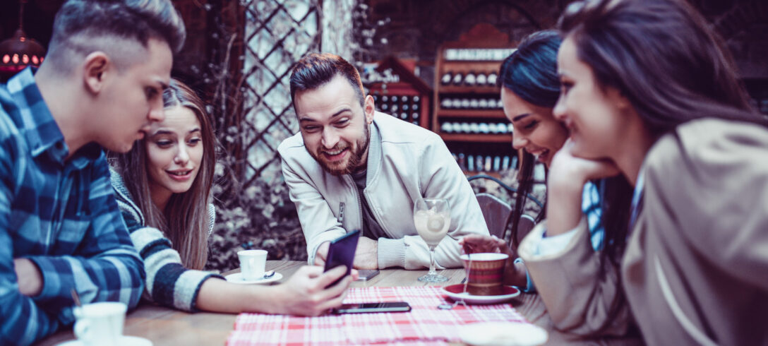 Groupe d'amis souriants regardant un smartphone dans un restaurant de café traditionnel